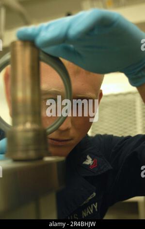 US Navy  Hull Maintenance Technician 2nd Class inspects a cuplink pipe as part of preventative maintenance. Stock Photo