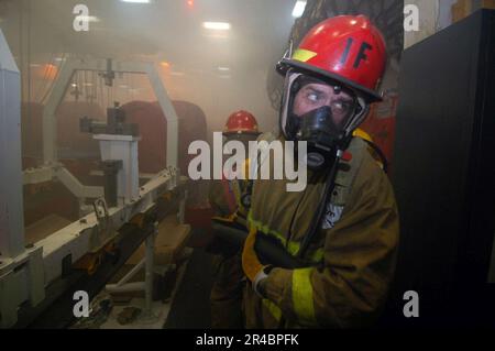 US Navy  A Sailor assigned to Repair Locker 1 Foxtrot relays a message from the hose team leader while combating a simulated fire. Stock Photo