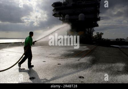 US Navy  Airman uses a fire hose and sprays off the flight deck after flight operations aboard the Nimitz-class aircraft carrier USS Ronald Reagan (CVN 76). Stock Photo