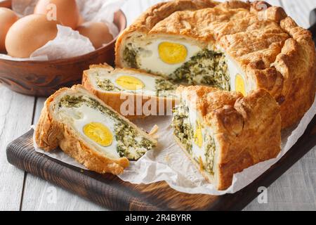 Portioned traditional Italian Easter cake or tart with spinach, ricotta and whole eggs closeup on the wooden board on the table. Horizontal Stock Photo