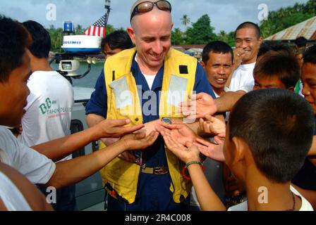 US Navy  Chief Warrant Officer hands-out candy to some of the townspeople from the small village of Leloan. Stock Photo