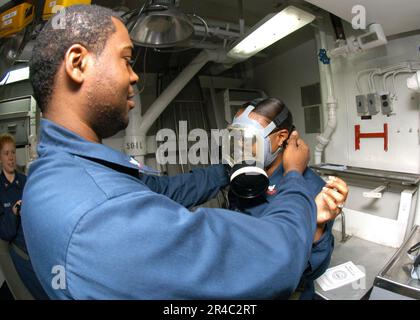 US Navy  Yeoman 3rd Class helps Yeoman 2nd Class adjust the straps on an MCU-2P gas mask during a Chemical, Biological, and Radiological (CBR) general quarters drill. Stock Photo