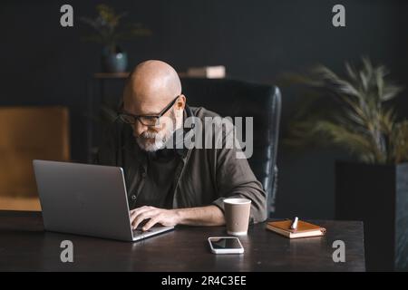 Hard worker concept, dedicated mid-aged man spends day immersed in work, diligently operating laptop with focus and determination. Commitment to job showcases professionalism and drive for success. High quality photo Stock Photo