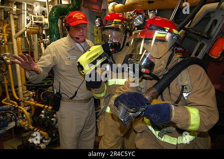 US Navy  Chief Machinery Repairman conducts training with a firefighting hose-team leader and nozzle man during a fire drill. Stock Photo