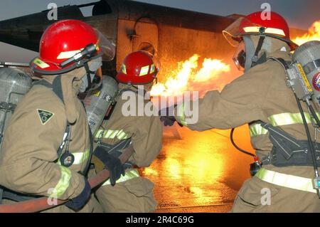 US Navy Aviation Electronics Technician 1st Class team leader of a shipUs repair locker, directs his hose team to advance on the Mobile Aircraft Firefighting Training Device (MAFTD) aboard USS Jo Stock Photo