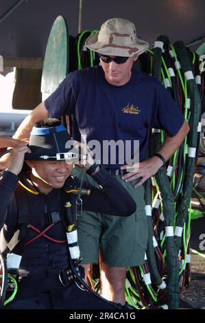 US Navy  Gunner's Mate 3rd Class watches Maj. from the Republic of Singapore Navy (RSN) don the neck dam prior to diving in the water. Stock Photo