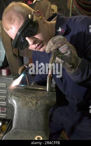 US Navy  Hull Technician 2nd Class bends the heated end of a metal rod to be used in making a replacement spoke in the steering wheel of a Rigid Hull Inflatable Boat (RHIB). Stock Photo