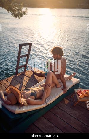 A young couple in swimsuit chatting while relaxing and sunbathing on the river bank on a beautiful summer day. Summer, river, vacation Stock Photo