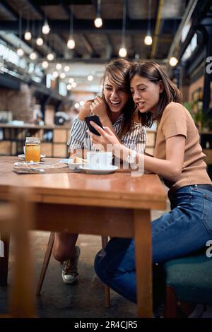 Two young beautiful girls in cafe having a great time. Woman showing something on her phone to her girlfriend. Fun, togetherness, lifestyle concept. Stock Photo