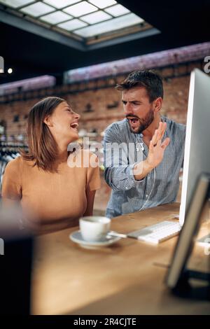 Two young business people, bloggers, sitting in modern office using desktop computer. Man and woman joyfully talking about project. Teamwork, business Stock Photo