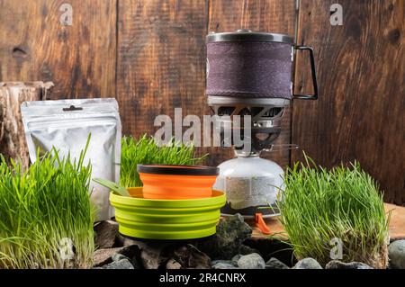 Travel utensils and gas stove on a wooden background. Multi-colored compact dishes for tourism. Stock Photo