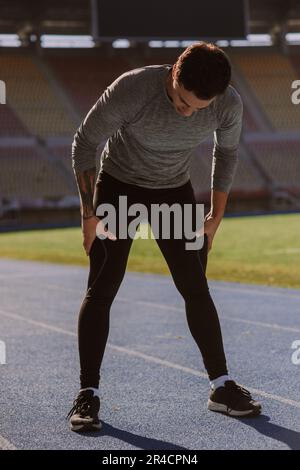 A tired male sports person is taking a break after exercising his legs. He was doing squats Stock Photo