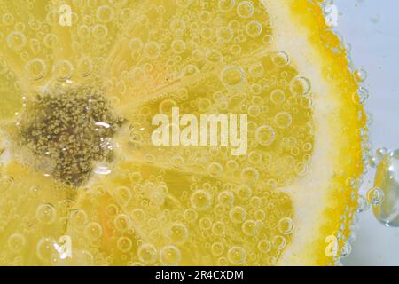 Slice of ripe lemon in water on white background. Close-up of lemon in liquid with bubbles. Slice of ripe citron in sparkling water. Macro image of Stock Photo