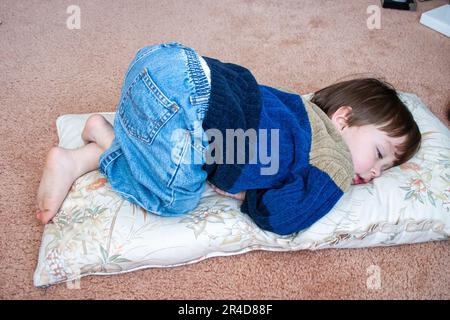 Child, boy, one year old, laying asleep on a cushion on the floor. Typical infant sleeping position, laying on his tummy with his bottom up in the air Stock Photo