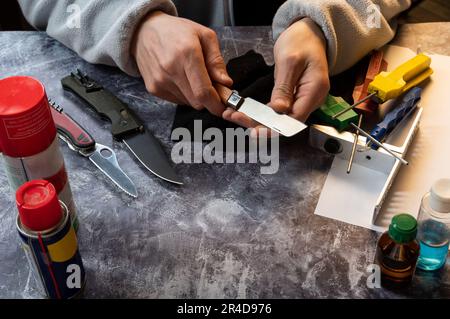Sharpening and caring for a knife. Checking a knife for sharpness. The master holds a sharp knife in his hands. View from above. Stock Photo