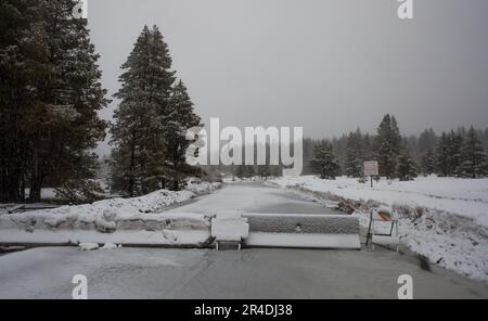 Snow-covered flooded sign with cone next to highway. Stock Photo