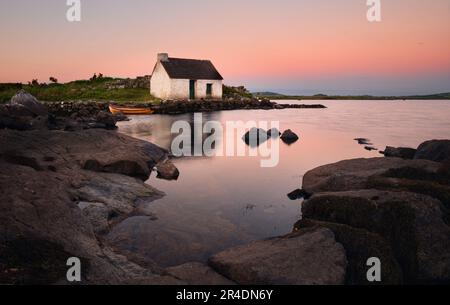 magical sunset scenery of fisherman's hut reflected in lake at Screebe, connemara national Park in County Galway, Ireland Stock Photo