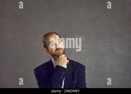 Portrait of puzzled and confused man with pensive facial expression against gray background. Stock Photo