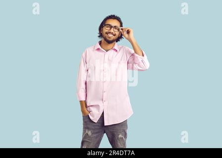 Young casual bearded Indian man student smiling adjusts glasses stands on turquoise background Stock Photo