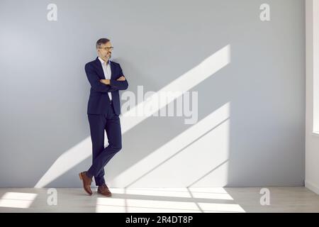 Middle aged handsome businessman leaning against gray wall Stock Photo