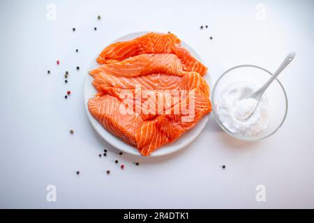 Fresh raw salmon fish fillet on a white plate, a small bowl of salt and black peppercorns on white background. Healthy food. Stock Photo
