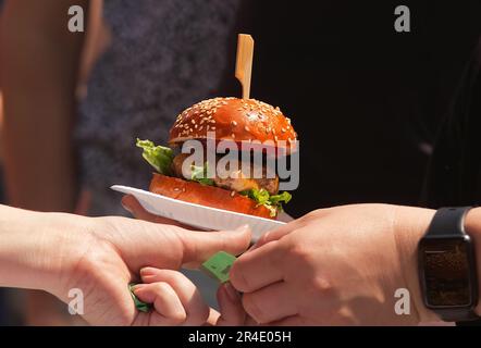 Selling burgers at a farmers street market. The customer hands the attendant a payment slip and takes the burger from her on a paper tray. Stock Photo