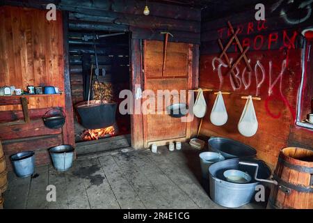 A large vat in which cheese is cooked over an open fire. The black cauldron is prepared over an open wood fire. Cheese factory in the mountains. Stock Photo