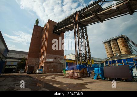Podolsk, Moscow province - August 02, 2021: Old Soviet factory buildings and silo. Trees grow on the roof. Wet road and blue sky. Stock Photo