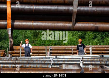 Podolsk, Moscow province - August 02, 2021: Pipes warehouse. Workers loads pipes on truck with overhead crane. Stock Photo