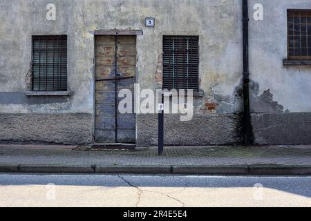 Pavement  on a street bordered by a worn out facade with windows and wooden doors in a village in the italian countryside Stock Photo