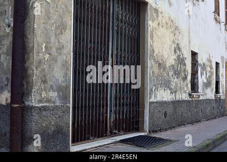 Pavement  on a street bordered by a worn out facade with windows and wooden doors in a village in the italian countryside Stock Photo