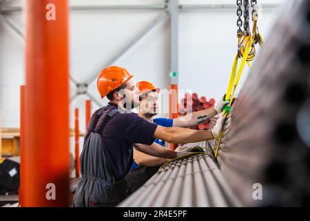 Podolsk, Moscow province - August 02, 2021: Pipes warehouse. Workers loads pipes with overhead crane. First man in focus. Stock Photo