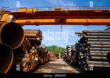Stack of steel pipes outdoor warehouse. Bridge crane on blue sky background Stock Photo