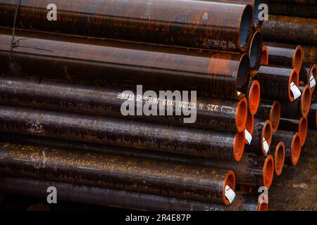 Wet rusty steel pipes with red plastic caps storing outdoor in rainy day Stock Photo