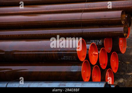 Wet steel rusty pipes with red plastic caps on outdoor warehouse in rainy day Stock Photo