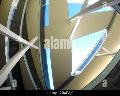 Image from below of a modern architecture building with a complex shape and pedestrian walkways. Reflective windows and the light blue sky in the back Stock Photo