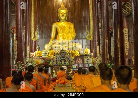 CHIANG MAI, THAILAND - NOVEMBER 04, 2014: Buddhist monks meditating in front of the Buddha image in Phan Tao Temple. Golden Buddha statue and buddhist Stock Photo