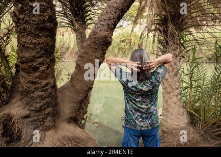 A gray-haired man stands among palm trees on the banks of a river, Greece, Crete, Preveli Stock Photo