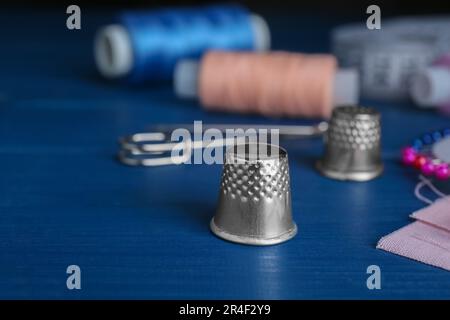 Silver thimble on blue wooden table, space for text. Sewing accessory Stock Photo
