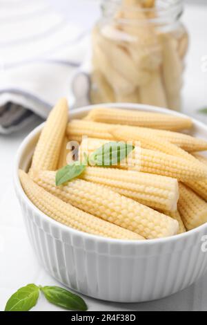Canned baby corns with basil on white tiled table, closeup Stock Photo
