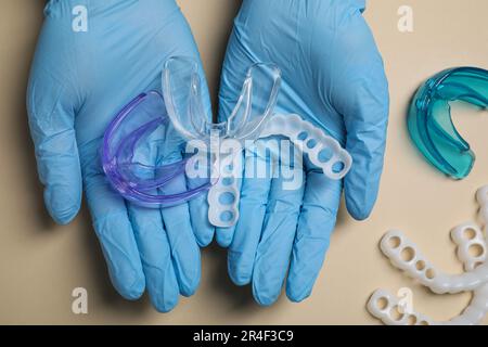 Bite correction. Dentist in medical gloves holding different mouth guards on beige background, top view Stock Photo