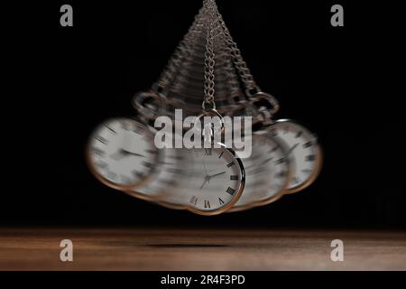 Hypnosis session. Vintage pocket watch with chain swinging over wooden surface on black background, motion effect Stock Photo