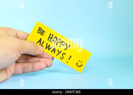 Choose happiness and be happy always reminder concept. Hand holding a bright yellow paper message note. Stock Photo