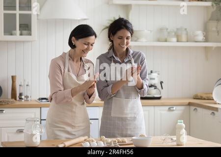 Cheerful positive mature mom and adult child woman baking pies Stock Photo