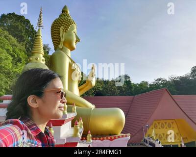 A young Thai woman taking a selfie in front of a Buddha statue at Wat Khao Rang, a Buddhist temple in Phuket, Thailand. Stock Photo