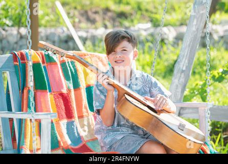 Musician child playing guitar. Kid boy singing and playing guitar outside. Kids music and songs. Stock Photo