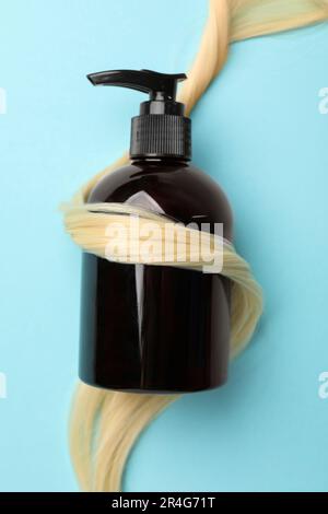 Shampoo bottle wrapped in lock of hair on light blue background, top view Stock Photo