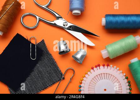Flat lay composition with thimbles and different sewing tools on orange background Stock Photo