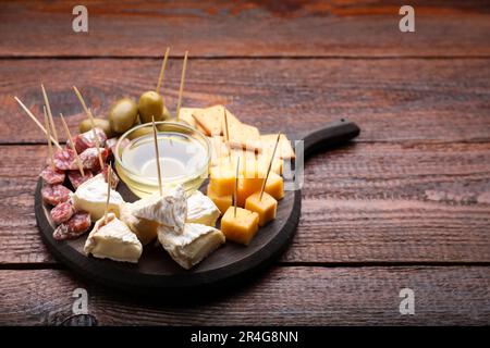 Toothpick appetizers. Pieces of cheese, sausage and honey on wooden table, space for text Stock Photo