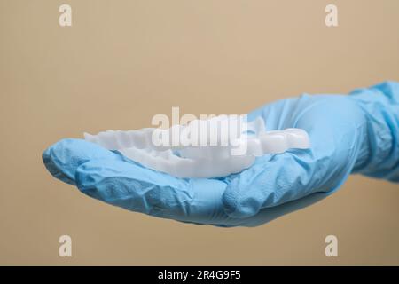 Bite correction. Dentist in medical glove holding mouth guards on beige background, closeup Stock Photo